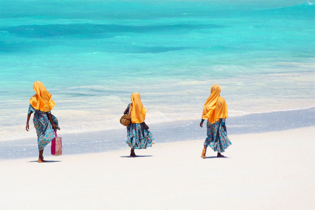 Trois femmes marchant sur la plage de Zanzibar aux eaux turquoise.