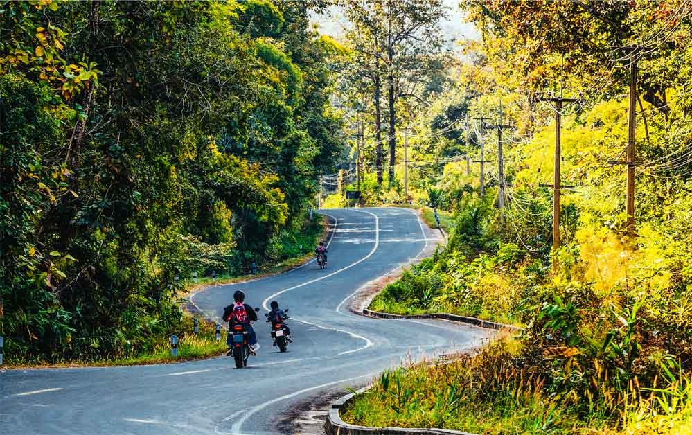 Trois motards sur une route thailandaise entourée d'une végétation luxuriante