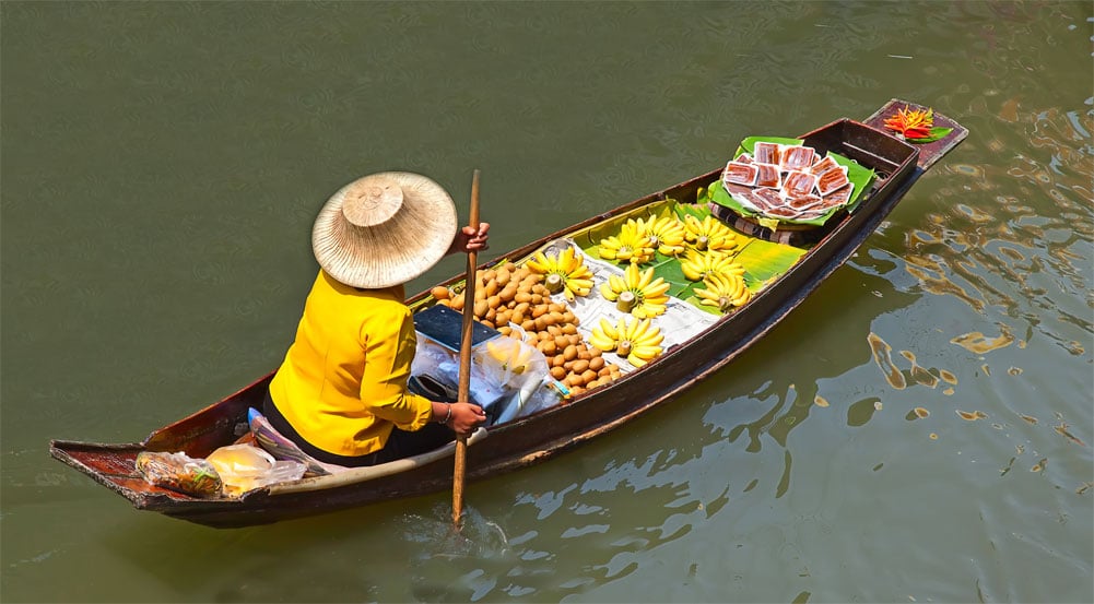 Un homme naviguant dans une embarcation avec un panier débordant de fruits.