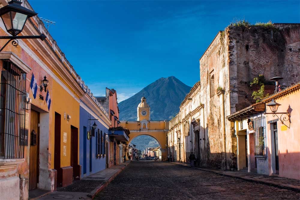 Les rues colorées de la ville d'Antigua, au Guatemala, avec un volcan qui se dresse à l'horizon.