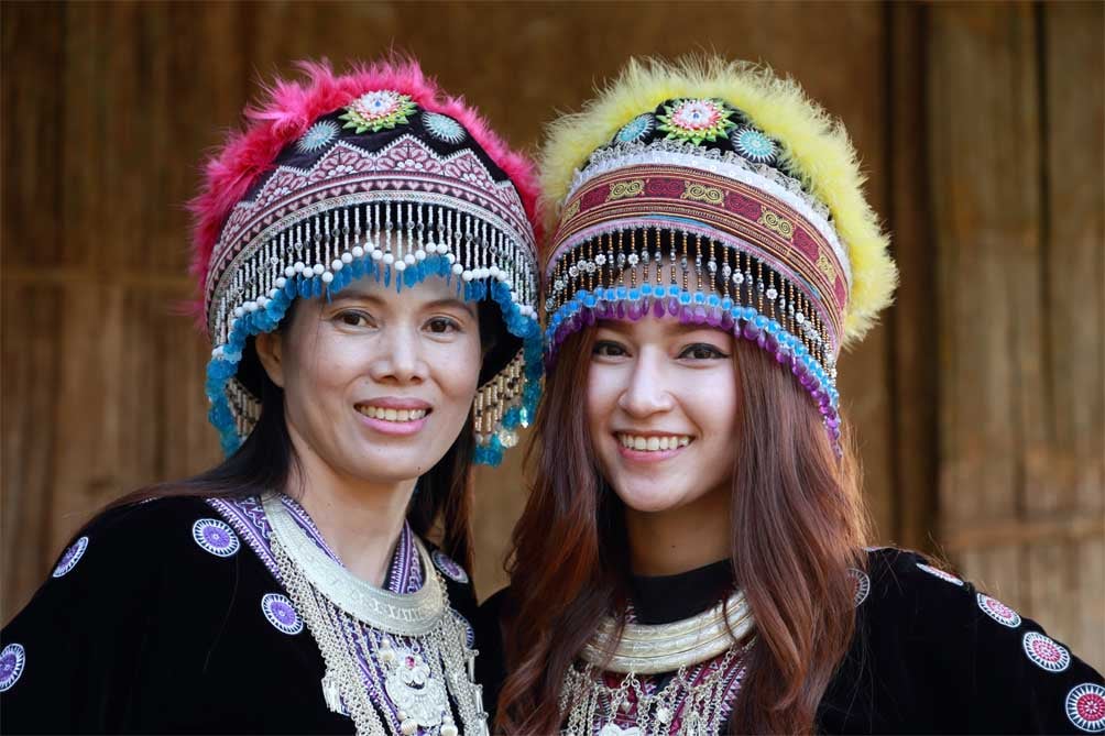 Deux femmes thaïlandaises en habits traditionnels et coiffées de chapeaux sourient pour la caméra.